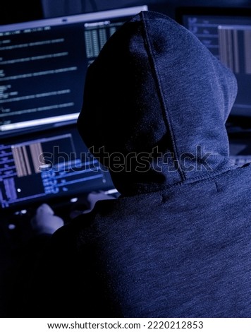 Hooded hacker attempting data breach at night in a dark private office, identity unknown
