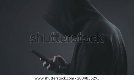 Hooded hacker using smartphone in dark environment, representing cybercrime, mobile hacking, data theft, and digital security threat, highlighting anonymous online activity and cybersecurity risk.