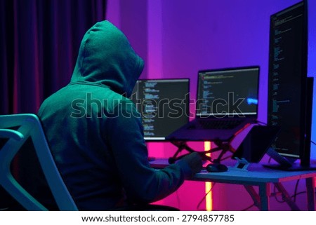 Hooded Hacker Working at Multiple Monitors in Dark Room