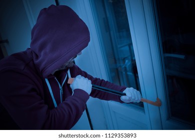 Hooded Housebreaker Forcing Window Lock To Make A Theft In A House At Night