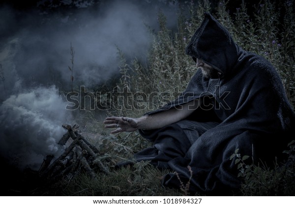 Hooded man wearing a cloak in a mysterious\
fantasy forest setting.