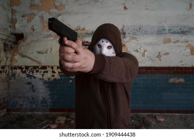 Hooded Robber With A Gun On Old Tiled Wall Background. Man Wear White Hockey Mask And Warm Pullover. 