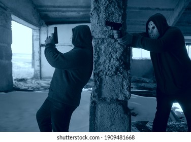 Hooded Robbers With A Gun On Old Tiled Wall Background. Men Wearing White Hockey Mask And Warm Pullover. 