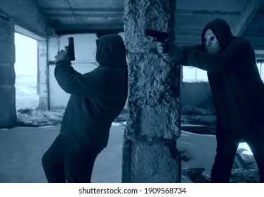 Hooded Robbers With A Gun On Old Tiled Wall Background. Men Wearing White Hockey Mask And Warm Pullover. 