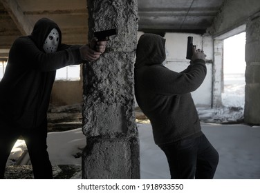 Hooded Robbers With A Gun On Old Tiled Wall Background. Men Wearing White Hockey Mask And Warm Pullover. 