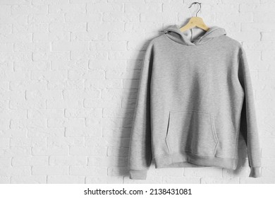 Hooded sweatshirt mockup. Blank grey hoodie on a hanger hung on a white brick wall. Hooded sweatshirt mockup.