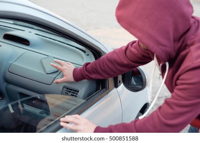 Hooded Thief Stealing A Mobile Phone From A Parked Car