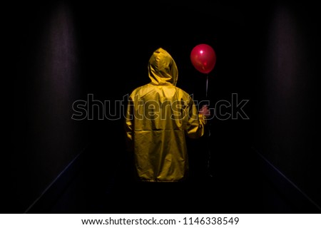 Hooded yellow figure with red balloon in dark creepy corridor