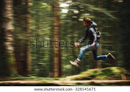 Hooded young man with backpack running in the forest