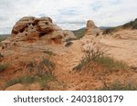 Hoodoos of Wyoming in summer.  Pockets of green grass with sandy hoodoos and pale muted sky.  Desert scrub on landscape with tan buttes.  High desert scenery of Wyoming countryside.  