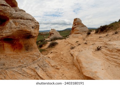 Hoodoos of Wyoming in summer.  Pockets of green grass with sandy hoodoos and pale muted sky.  Desert scrub on landscape with tan buttes.  High desert scenery of Wyoming countryside.  