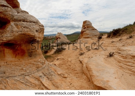 Hoodoos of Wyoming in summer.  Pockets of green grass with sandy hoodoos and pale muted sky.  Desert scrub on landscape with tan buttes.  High desert scenery of Wyoming countryside.  