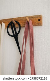 Hook hanger with pink eco bag and black scissors hanging on a white wall in the modern kitchen. Storage ideas. 