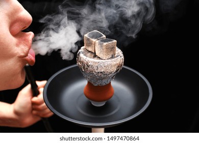 Hookah Bowl With Foil, Embers, Saucer And Part Of The Face Of A Smoking Person Blowing Smoke On A Black Background