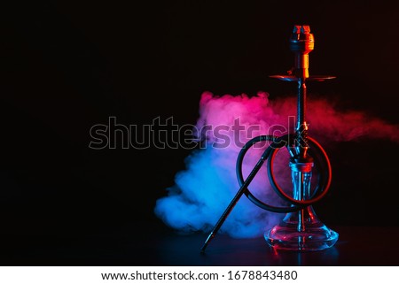 hookah with a glass flask and a metal bowl shisha with colored smoke on the table on a black background with a copy space