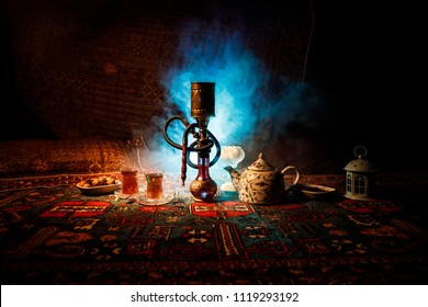 Hookah hot coals on shisha bowl making clouds of steam at Arabian interior. Oriental ornament on the carpet eastern tea ceremony. Stylish oriental shisha in dark with backlight. Selective focus
