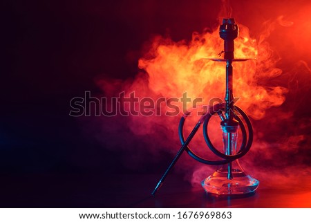 hookah shisha with glass flask and metal bowl with colored smoke on a black background. Traditional Eastern vacation for relaxation