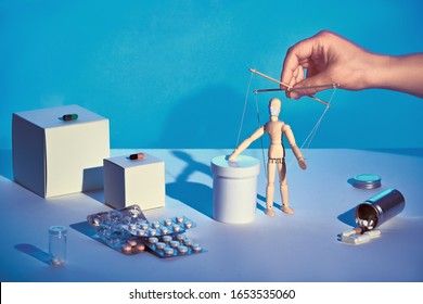 Hooked on medicine. Sinister hand controlling wooden puppet among various medications, pills, capsules. Bevare of fake news about medications to cure COVID-19, novel coronavirus.