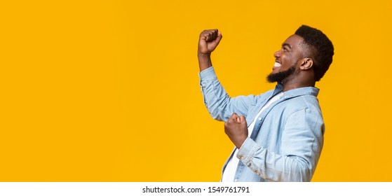 Hooray. Happy african american man raising fists in the air, celebrating success over yellow background with free space