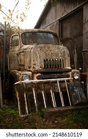 Hope, BC, Canada, April 14 2022: Old rundown trucks parked behind a dirty yard and shed with garage, grungy and filthy, disused and in disrepair, small down industrial, brown grime and moss covered