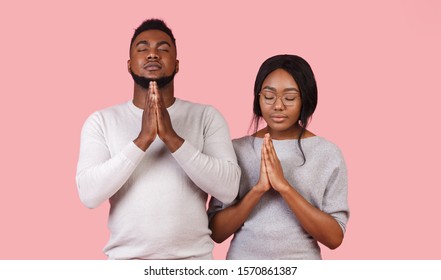 Hope For Good Luck. Young Black Couple Folded Their Hands In Front Of Them And Praying With Closed Eyes, Pink Background