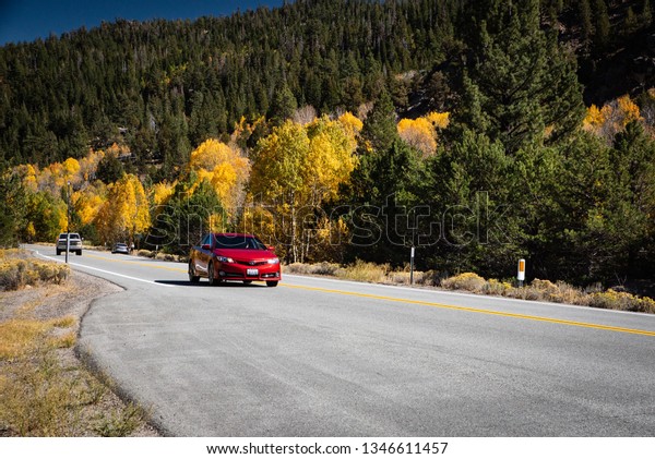 HOPE VALLEY, CA/U.S.A. - SEPTEMBER 29, 2018:\
Horizontal orientation photo of red Toyota driving on Highway 88 in\
the Hope Valley, California with aspens changing color in the fall\
in the background.