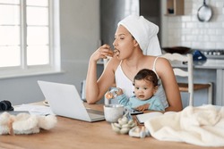 Hope Youre Having A Good Morning Because I Have A Busy One. Shot Of A Woman Eating Rusks While Working On Her Laptop And Holding Her Baby On Her Lap.