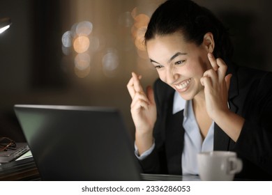 Hopeful businesswoman crossing fingers in the night at office or home - Powered by Shutterstock