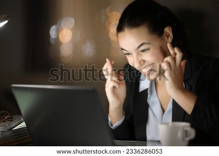Hopeful businesswoman crossing fingers in the night at office or home