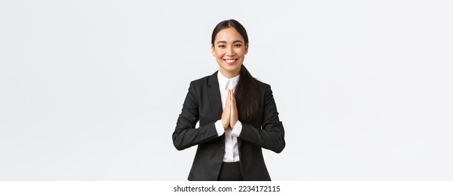 Hopeful glad asian businesswoman in black suit bowing politely and say namaste, greeting clients and smiling friendly. Thankful female manager thanking for help, being grateful, appreciate help.