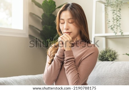 Hopeful make wish, calm asian young woman belief, hand in prayer, sitting meditating on sofa at home, Christian girl praying to God for ask, request with closed eyes dreaming for help, thank you God.