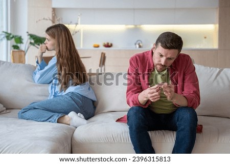 Hopeless depressed woman desperately looking at window while man with indifferent face expression examines nails demonstratively ignoring wife. Toxic relations, disagreement, relationship problems