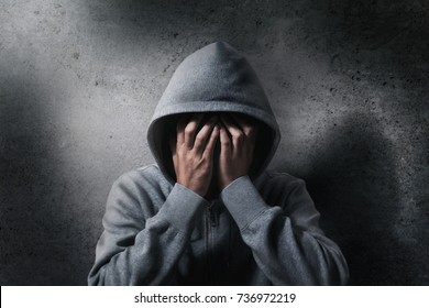 hopeless drug addict going through addiction crisis, portrait of young adult man is covering his face as wearing hood after abusing medicine and drug