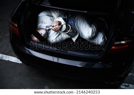 Hoping for a miracle. A bound and blindfolded businessman lying in the trunk of a car.