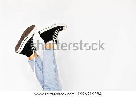 Hoprizontal shot of cool sneakers, female legs wearing white socks and snickers, blue jeans model legs isoalted over white background for catalog, sporty woman legs against studio waal. Sport concept.