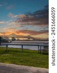 The Horace Wilkinson Bridge over the flowing waters off the Mississippi River with boats on the water, lush green grass and clouds at Louisiana Memorial Plaza in Baton Rouge Louisiana USA