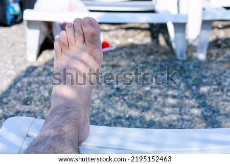 Horizantal view of male foot resting on sunbed in the lights of the setting sun after a walk in the sandy beach. One male foot covered on the beach. Family summer vacation concept. 