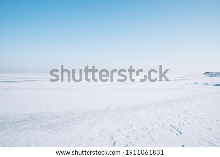 horizon of the frozen sea on the ice a lot of snow blue sky no clouds bright day on the horizon you can see a little coast and forest footprints in the snow footpath from people