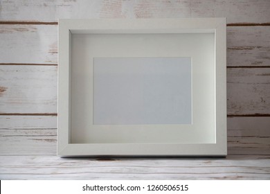 A Horizontal 5x7 White Frame And A White Wooden Background.