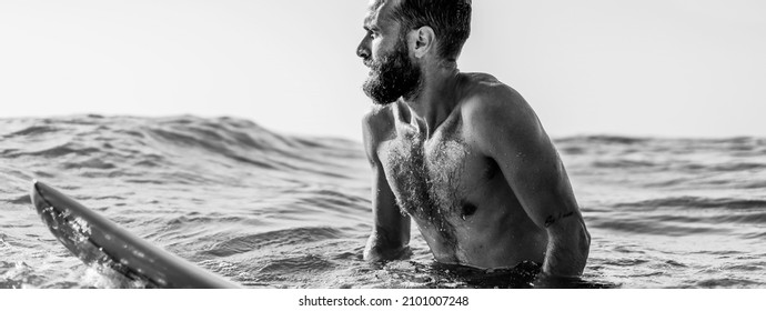Horizontal banner or header with hipster surfer sitting on his surfboard into the ocean water and waiting for a big wave - Fit bearded man training with surfboard to sea