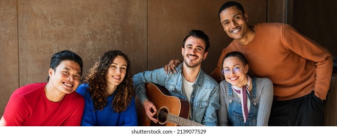 Horizontal banner or header Multiracial group of young friends portrait. People looking at the camera with smile, one is playing guitar. - Shutterstock ID 2139077529