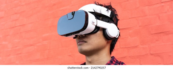 Horizontal banner or header with portrait of young oriental man using 3d viewer with headphones outdoor - Metaverse, fictional world and virtual reality concept