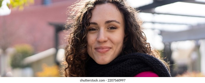 Horizontal banner or header with smiling girl with wavy hair standing outdoor with urban city context as background - Millennial or gen z woman having fun outdoor during winter season - focus on eyes - Shutterstock ID 2207560997