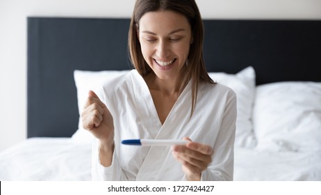 Horizontal banner image of awakened millennial woman sitting in bed holding digital pregnancy test focus on happy excited face, check ovulation period, fertility maternity, new life baby birth concept