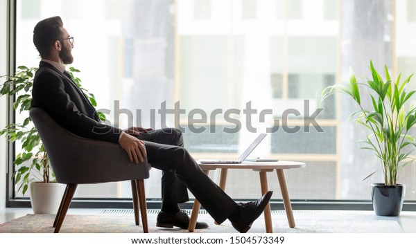 Horizontal banner middle eastern ethnicity\
businessman sit on armchair resting in modern room looks out window\
thinking about prosperous his own company plan future projects,\
business vision\
concept