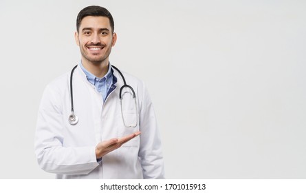 Horizontal banner of smiling young male doctor showing and presenting something with hand, isolated on gray background with copy space on the right side