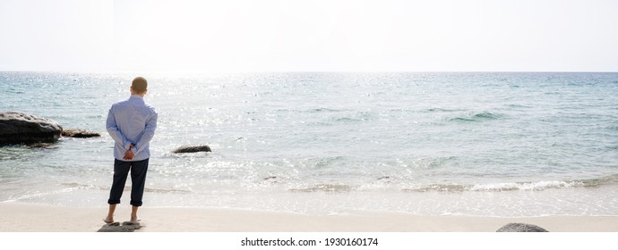 Horizontal banner with Unrecognizable man wearing business suit standing on the shore in a beautiful Italian beach looking at the horizon. Meditation, relaxation, escape from city life concept.