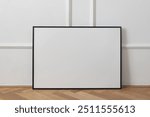 Horizontal black thin picture frame mockup. Empty wooden frame poster mock-up template on oak wooden parquet floor. White wall background, stucco moulding decor, minimal Scandinavian interior.