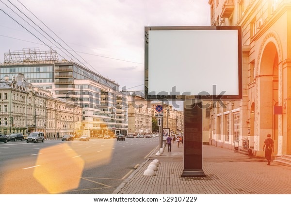 Horizontal blank\
billboard on the city street. In the background buildings and road\
with cars. Film effect. Mock\
up.