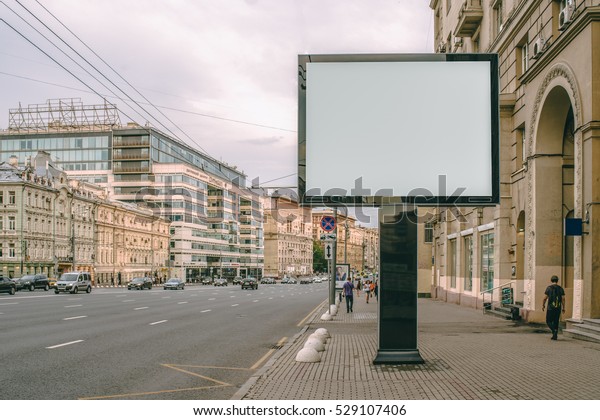 Horizontal blank billboard on the city street.\
In background buildings and road with cars. Mock up. The poster on\
the street next to the\
roadway.